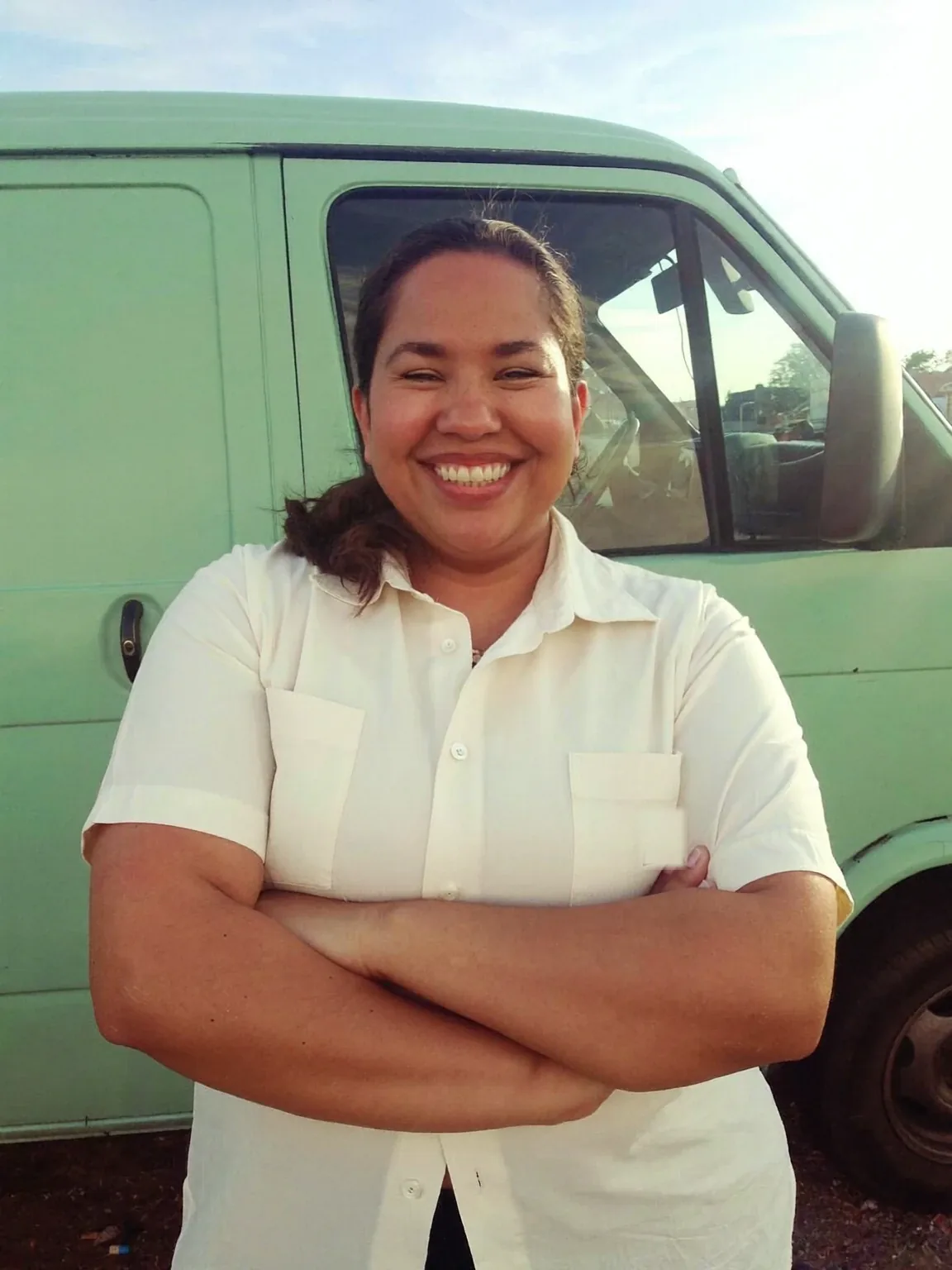 Maria Constanza, owner of Ivory Maids, smiling with her arms crossed in front of a mint-green van